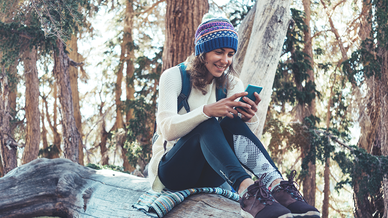 Woman hiking sitting on log looking at smart phone.