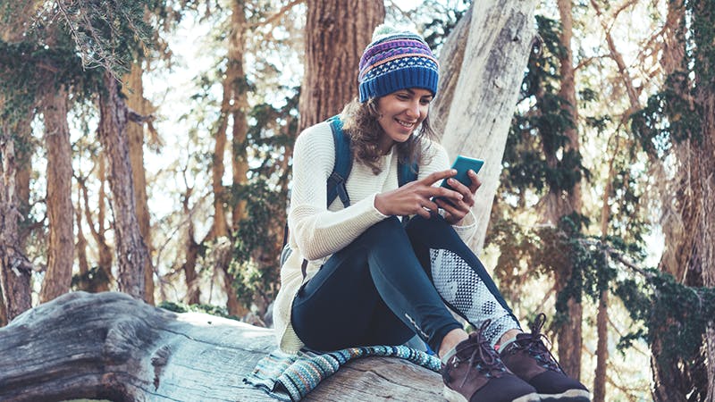 Woman hiking sitting on log looking at smart phone.