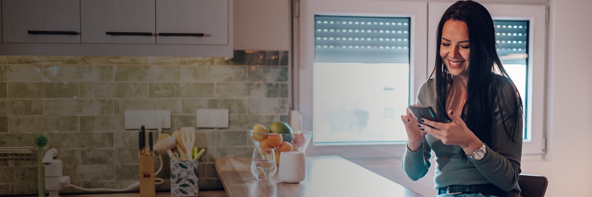 Woman at kitchen island looking at phone and smiling