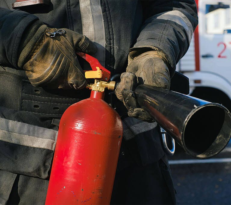 A firefighter holds a red fire extinguisher in front of a fire truck.