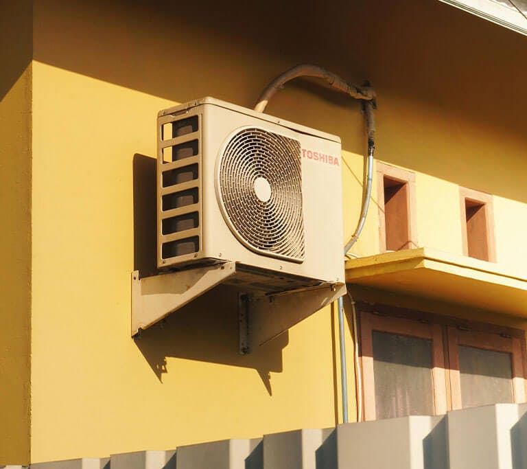 A yellow house with a white fence and a very old Toshiba air conditioning unit.