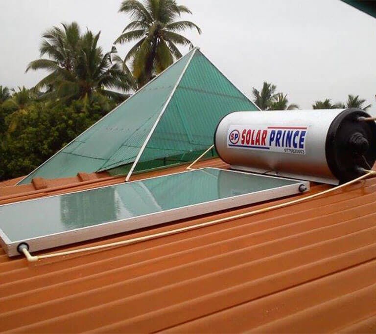 A solar water heater labeled “Solar Prince” is sitting on an orange roof next to its panel in a location with palm trees in the background on a cloudy day.