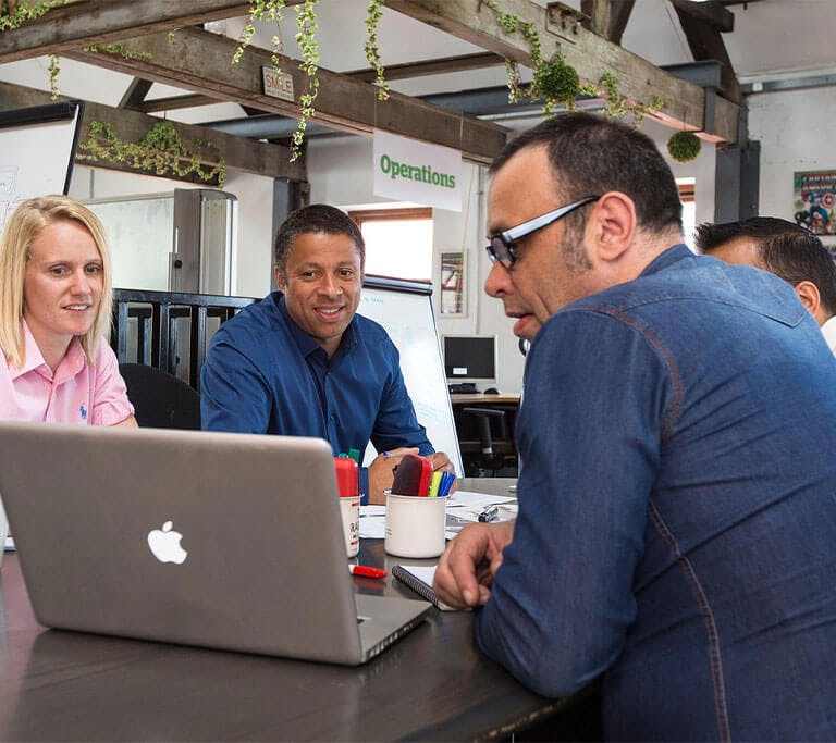 Work group sitting at a table gathered around a laptop.
