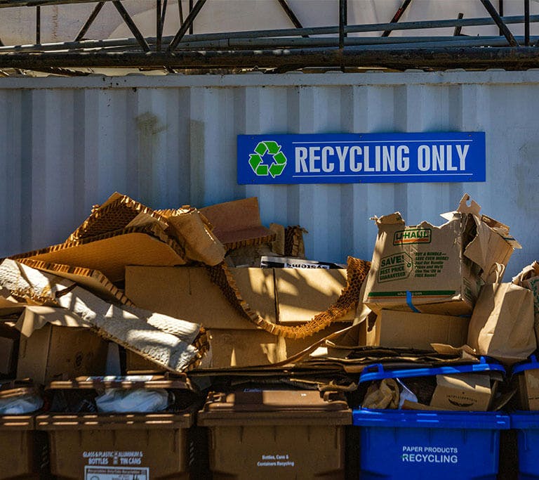 Cardboard boxes pile up in recycling bins beneath a “Recycling Only” sign.