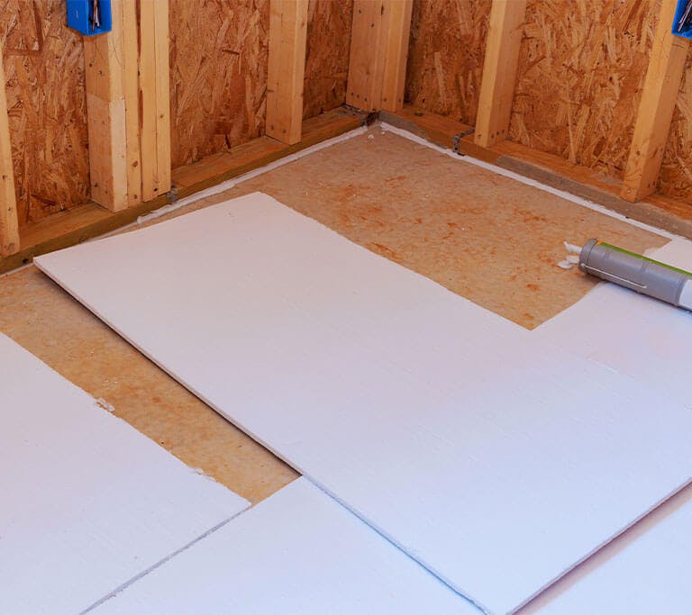 Two sheets of floor insulation are leaning against exposed wooden support beams in an unfinished basement.