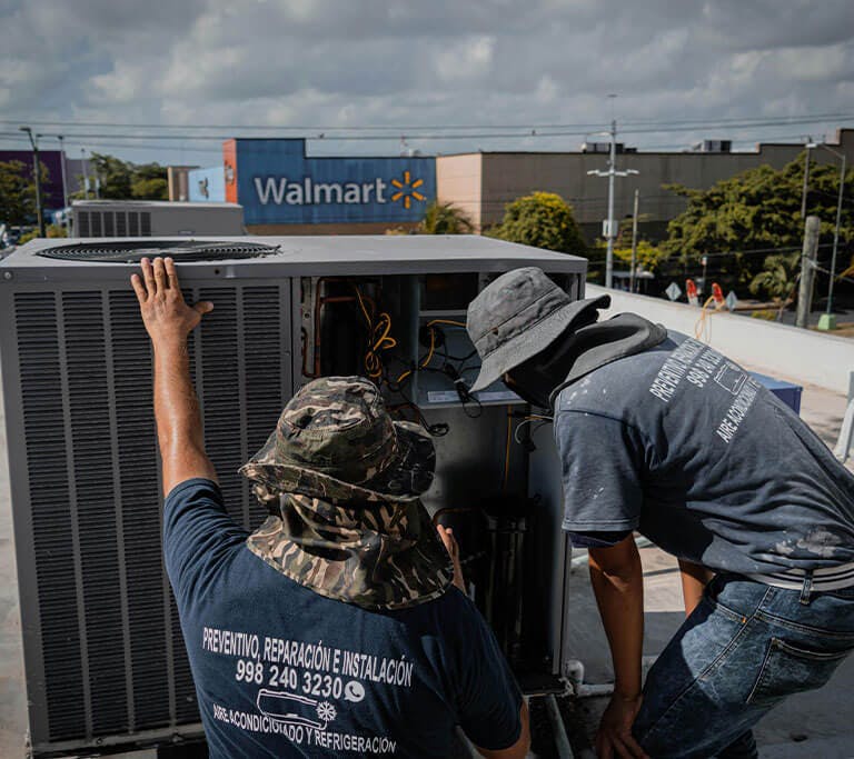 Two men service an air conditioning unit atop a roof near a Walmart and a DQ.