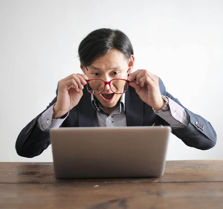 A man makes a shocked face while looking at a laptop screen.