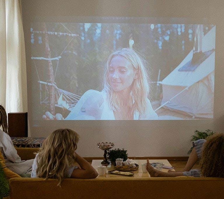 A group of friends sits in a living room and streams a movie on a giant projector screen.