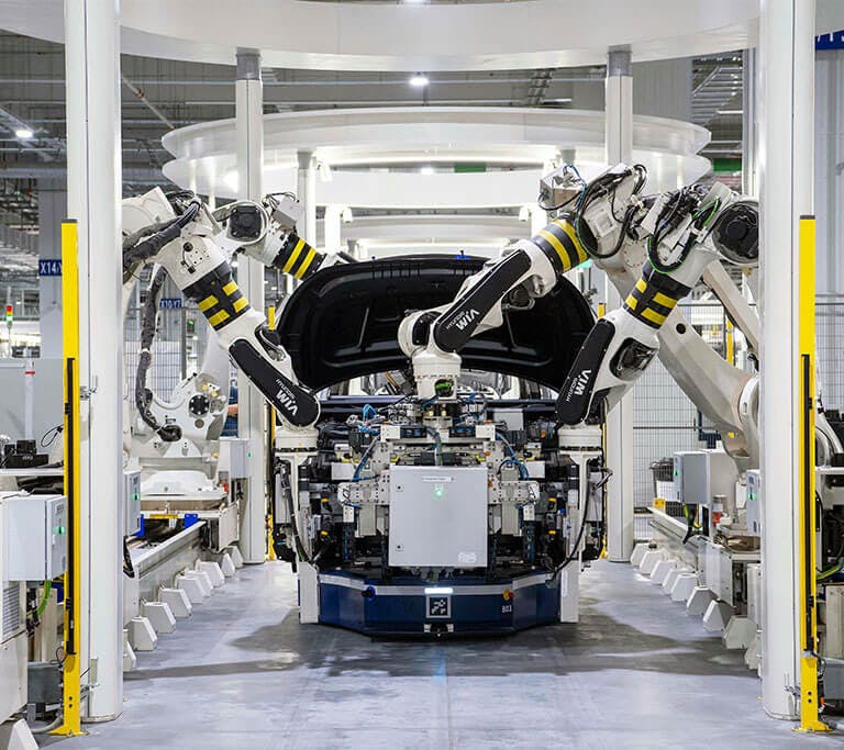 A modern automotive manufacturing plant with robotic arms assembling a vehicle. The car’s hood is open as multiple robotic arms equipped with tools work simultaneously on different parts of the vehicle.