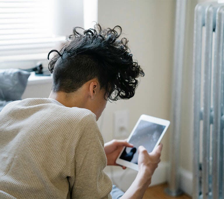 Person sitting next to a radiator inside their home checking an air quality monitor app on their tablet.