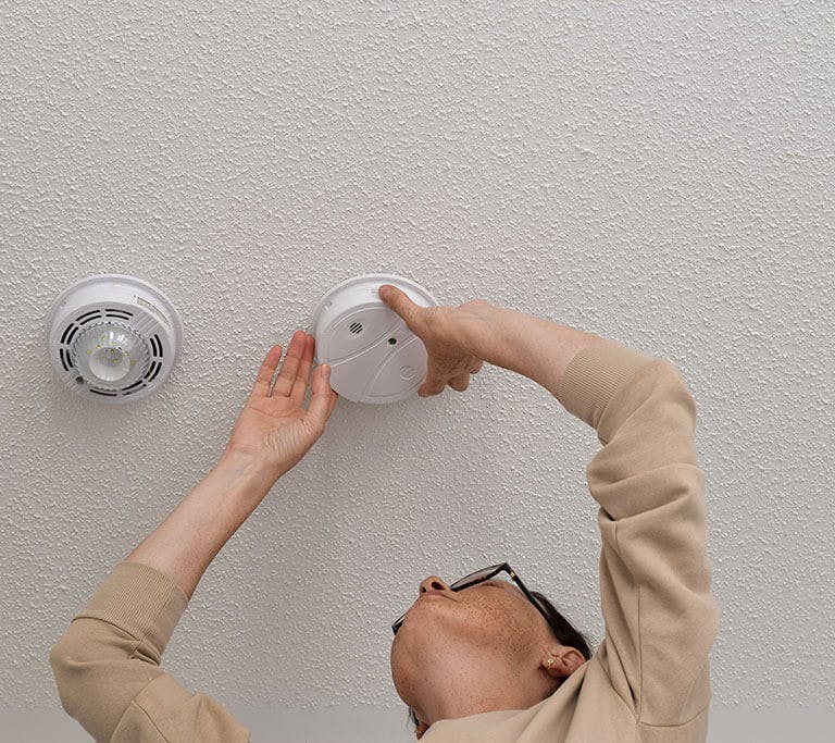 A person installing a carbon monoxide detector on ceiling