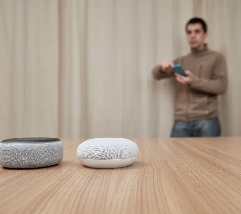 Man comparing Amazon Echo Dot, and Google Nest