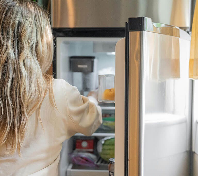 A person opens a silver fridge, revealing several out-of-focus food items.