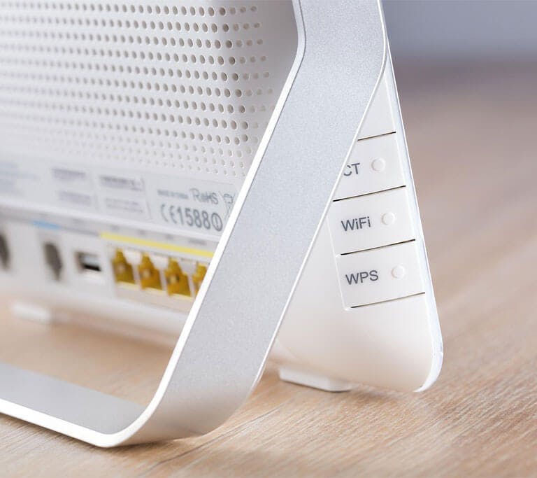 Close-up of a white wireless router with visible ethernet ports and WIFI, WPS buttons on a wooden desk.