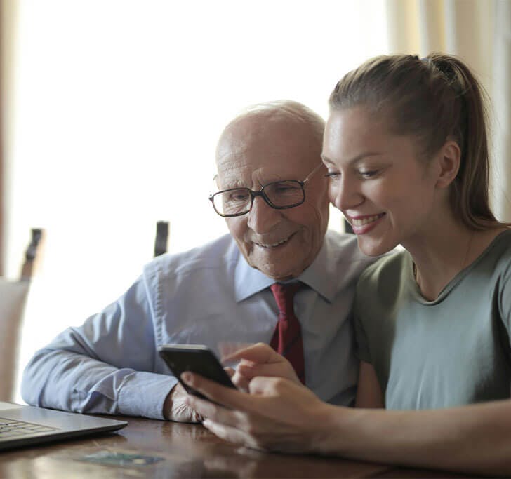 A man and woman using a laptop and smartphone while smiling.