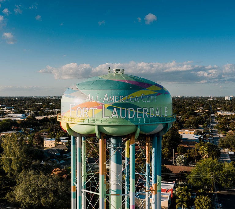 A painted Fort Lauderdale water tower towers over homes and businesses under a blue sky.