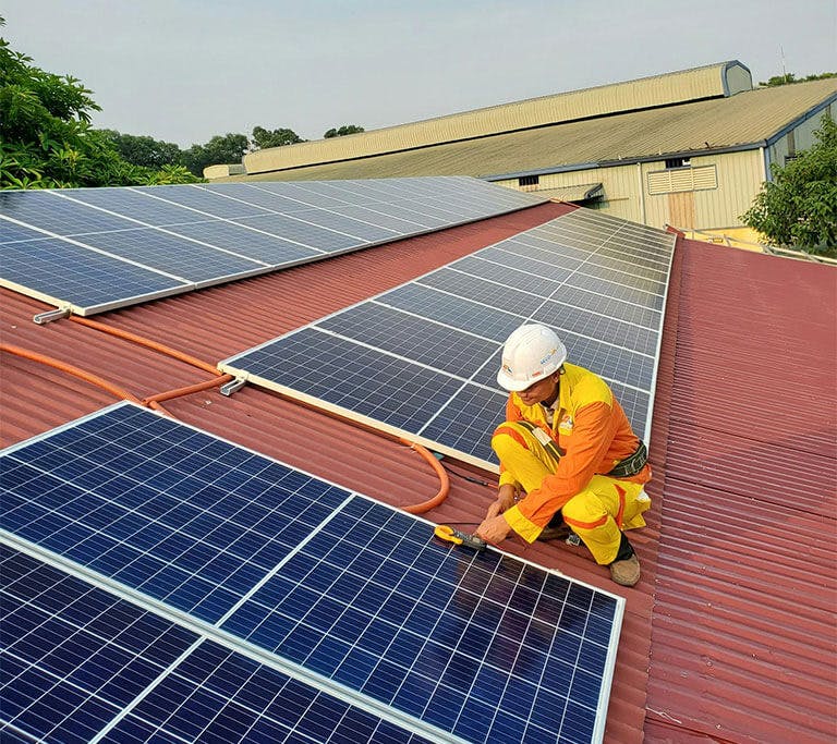 A man in construction clothing uses tools while installing a solar panel on a roof.