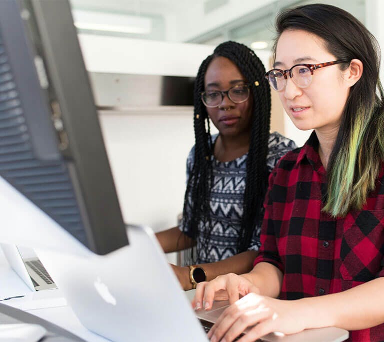 A woman wearing a read and black checkered shirt using a MacBook.