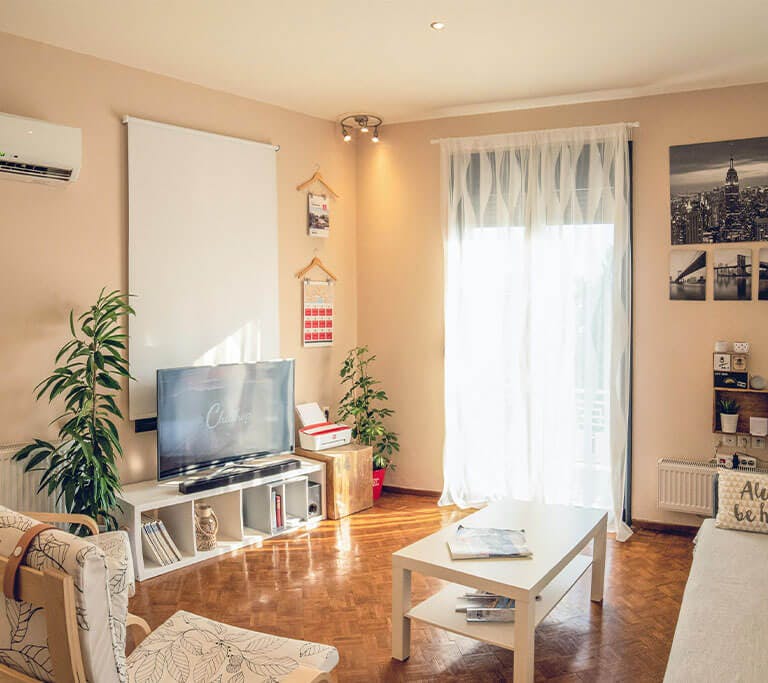 A modern mini-split air conditioning system controls the temperature of a warmly decorated living room with peach walls and white, minimalist decor.