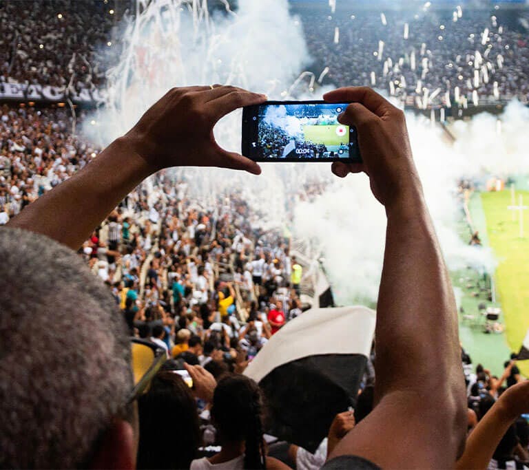 A person attending a large sporting event holds up their smartphone to record video.