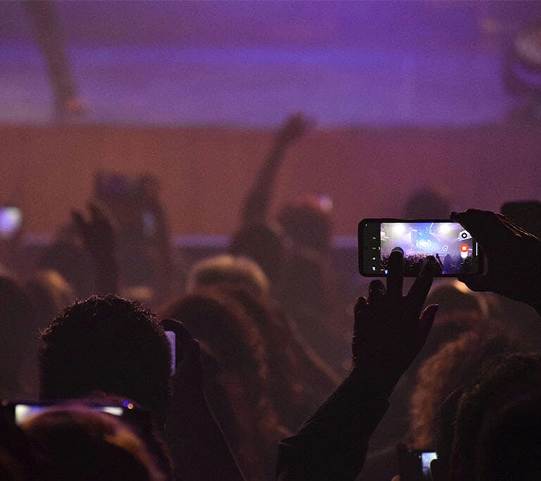 People in a crowd use their mobile phones to take photos at a festival event or concert.