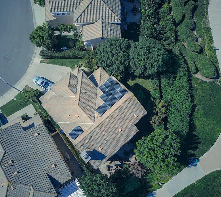 An aerial view of a beautiful neighborhood with green walkways, trees and solar panels on the rooftop of the home in the center.