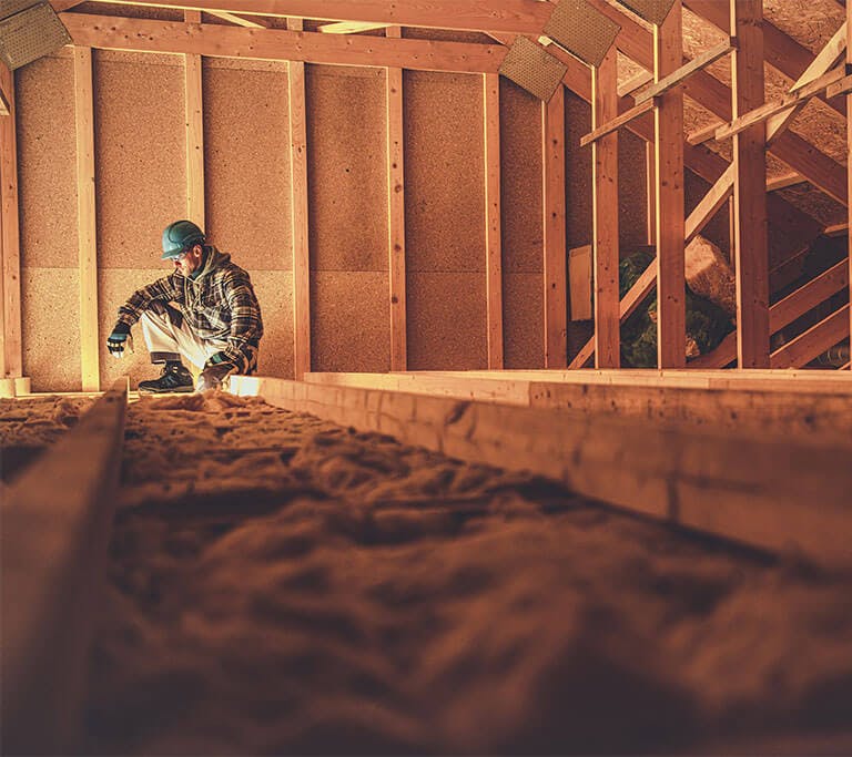 An unfinished attic with wooden beams and brick walls is in the process of having its floor insulated with loose-fill cellulose insulation.