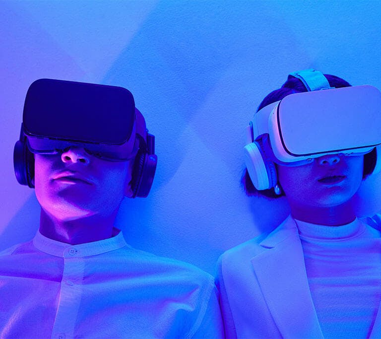 Two people wearing futuristic, minimalist fashion and virtual reality (VR) headsets lean against a white background, fully immersed in VR.