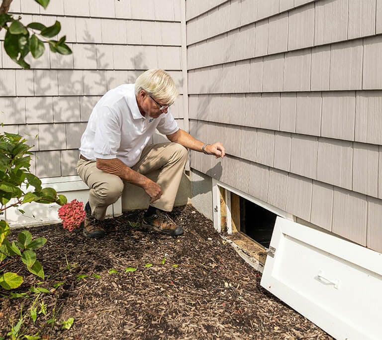 An energy expert inspects the crawlspace of home with grey siding.