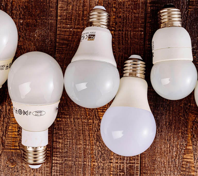 Six energy-saving LED light bulbs are arranged in a row across a wooden surface.
