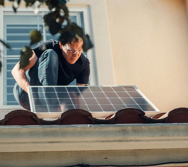 A man carefully places a solar panel down on to a roof.
