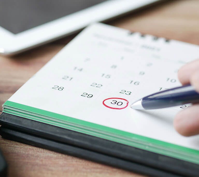 A close-up of a desk calendar with a circled date, next to a laptop and keyboard.
