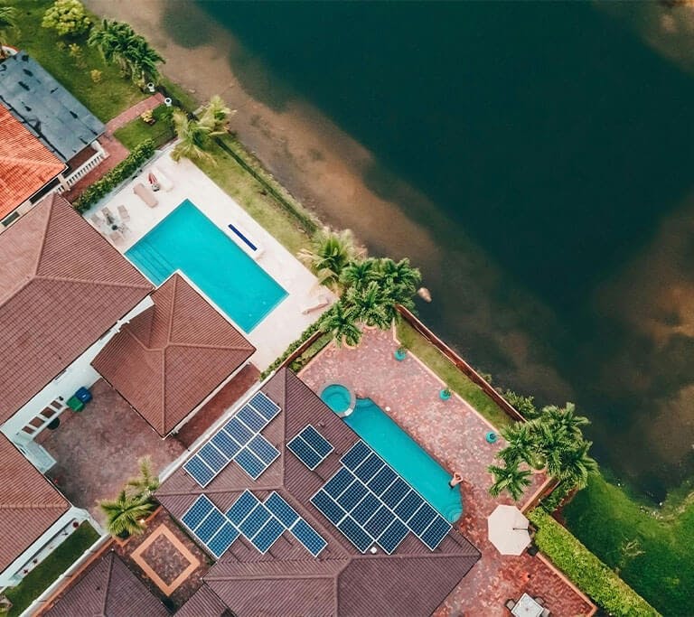 Top view of houses with swimming pools, palm trees and solar panel installations.