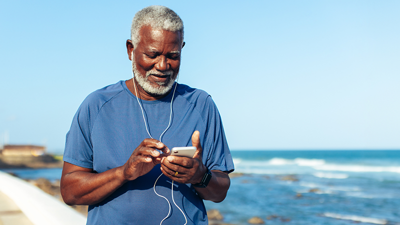 Man on a beach looking at his smart phone with headphone in