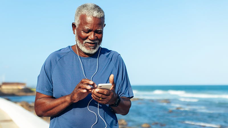 Man on a beach looking at his smart phone with headphone in