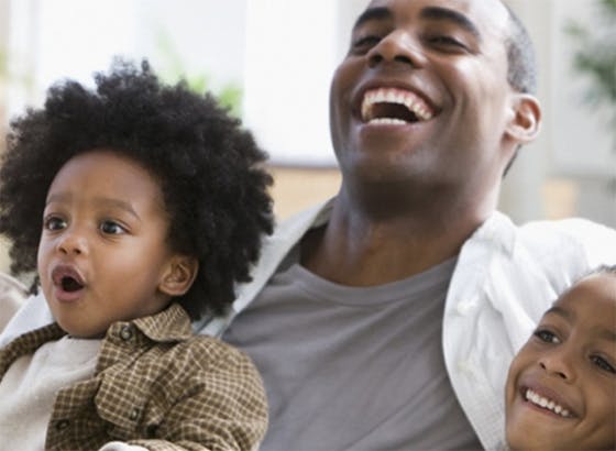 Father and young sons laughing and watching television together