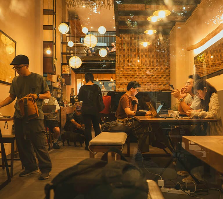 A busy café with people using laptops, mobile devices and point-of-sale systems at shared tables.
