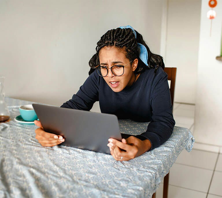 Person sitting at a table looks concerned while using a laptop, appearing to troubleshoot a computer issue.