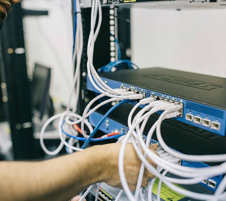 A person working on a network server rack, connecting or adjusting multiple Ethernet cables plugged into networking equipment.