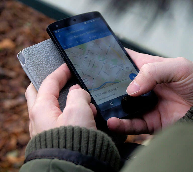 A person’s hands are holding a mobile phone as they interact with a maps app.