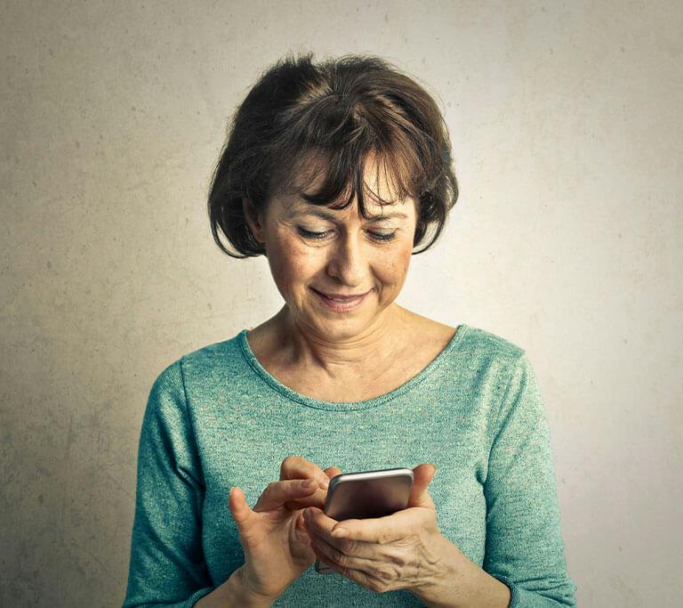 Person smiling while using a smartphone indoors against a plain background.