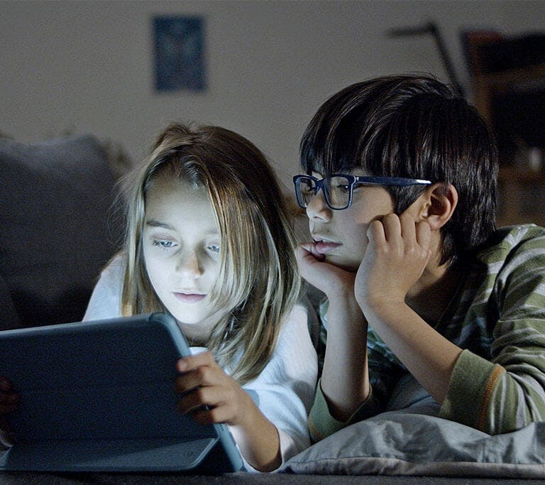 Children using a tablet in bed at bedtime, representing offline video downloads and family screen time.