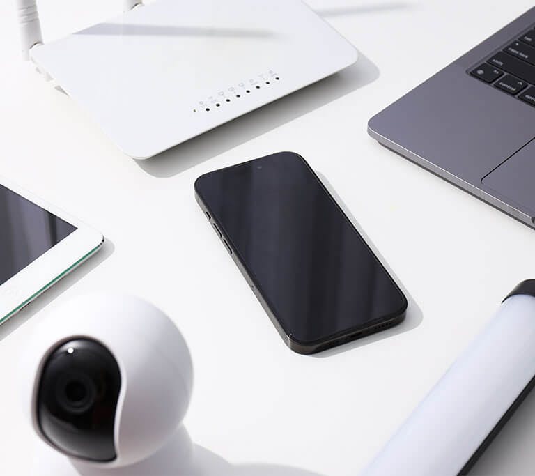 Photograph showing a laptop, smartphone, and a Wi-Fi router arranged on a white surface against a light background.