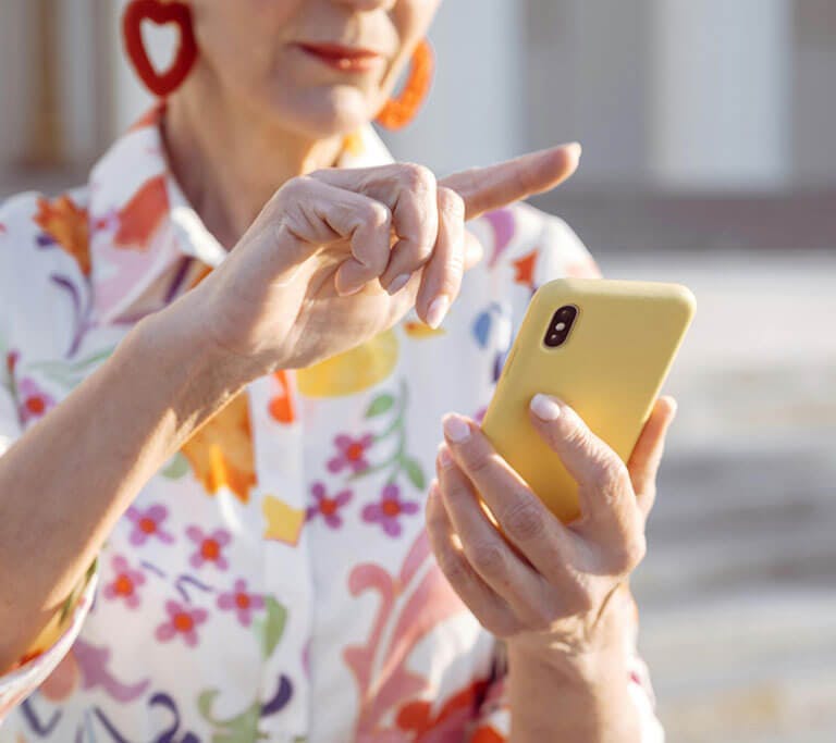 A person wearing a white button-up shirt with flowers on it uses a smartphone with a yellow case.