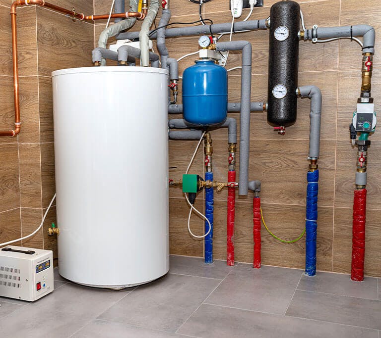 A condensing boiler in a brick room with an indirect water heater connected to pipes that distribute heat to radiant floors and cast-iron radiators.