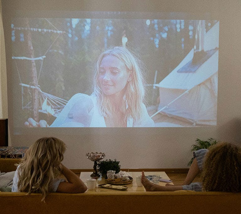 Four friends sit on sectional sofas while streaming a movie on a projector screen.