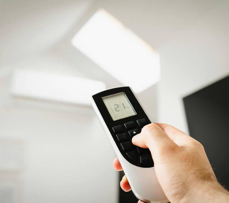 A person holding a remote control aimed at a smart thermostat in a bright room.