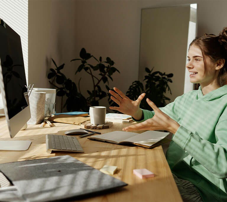 Person works at a home desk while engaging in a video call on a desktop computer.