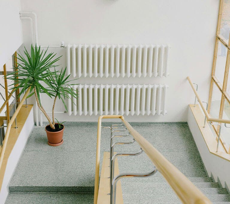 Staircase with metal railings in multistory house with a radiator in the background that uses water heated in a boiler to provide warmth.