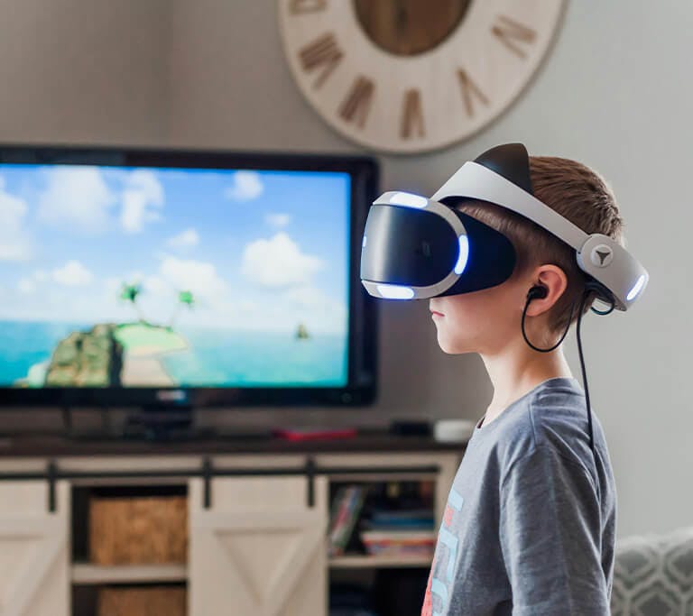 A child in a living room wears a VR headset in front of a TV that’s displaying a video game set on a small island.